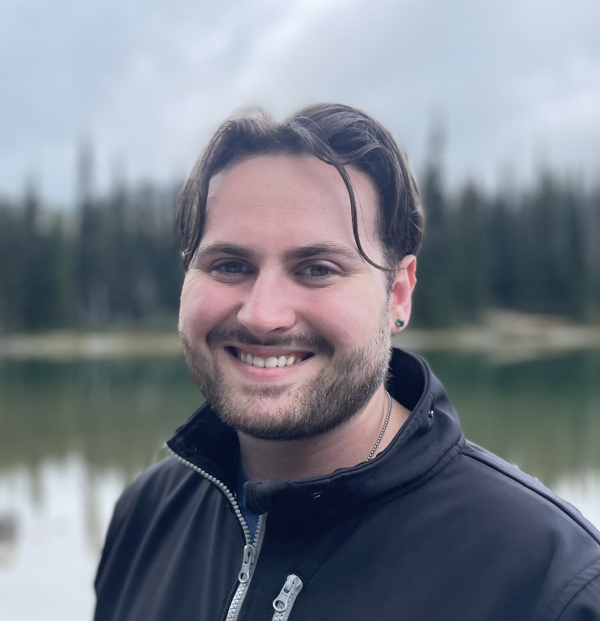 This image of UW Tacoma senior, Austin Donovan, is a casual headshot framed by a small lake and blurred pine trees.